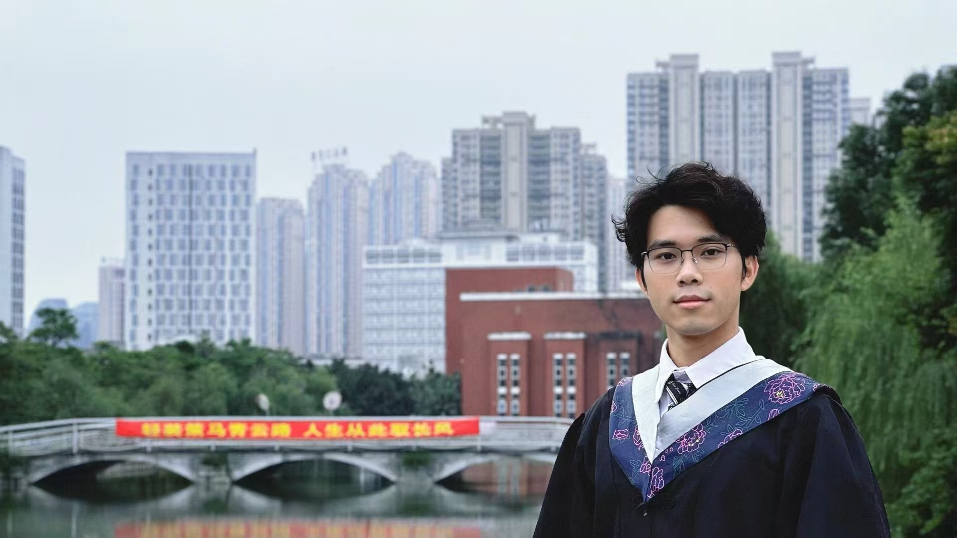 Graduation photo on the bridge over Xingyu Lake at Fujian Normal University, with the banner "轻装策马青云路，人生从此驭长风" in the background.